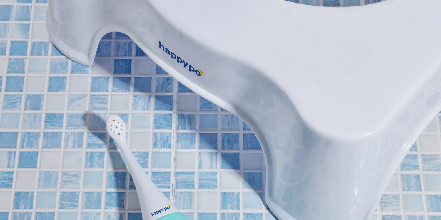 A HappyPo bottle lying on blue mosaic tiles beside a white step stool