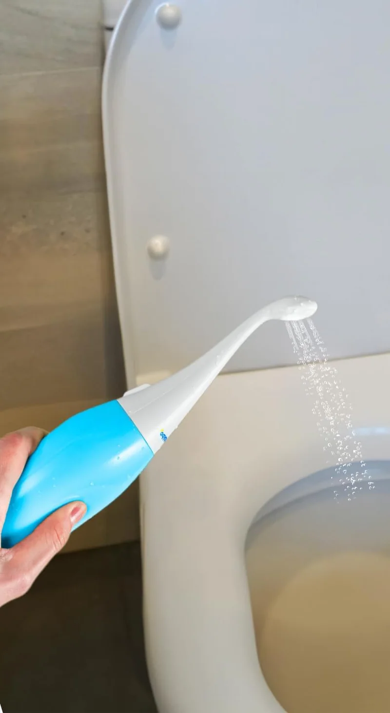 A light blue HappyPo bottle held nozzle-up, spraying a fine jet